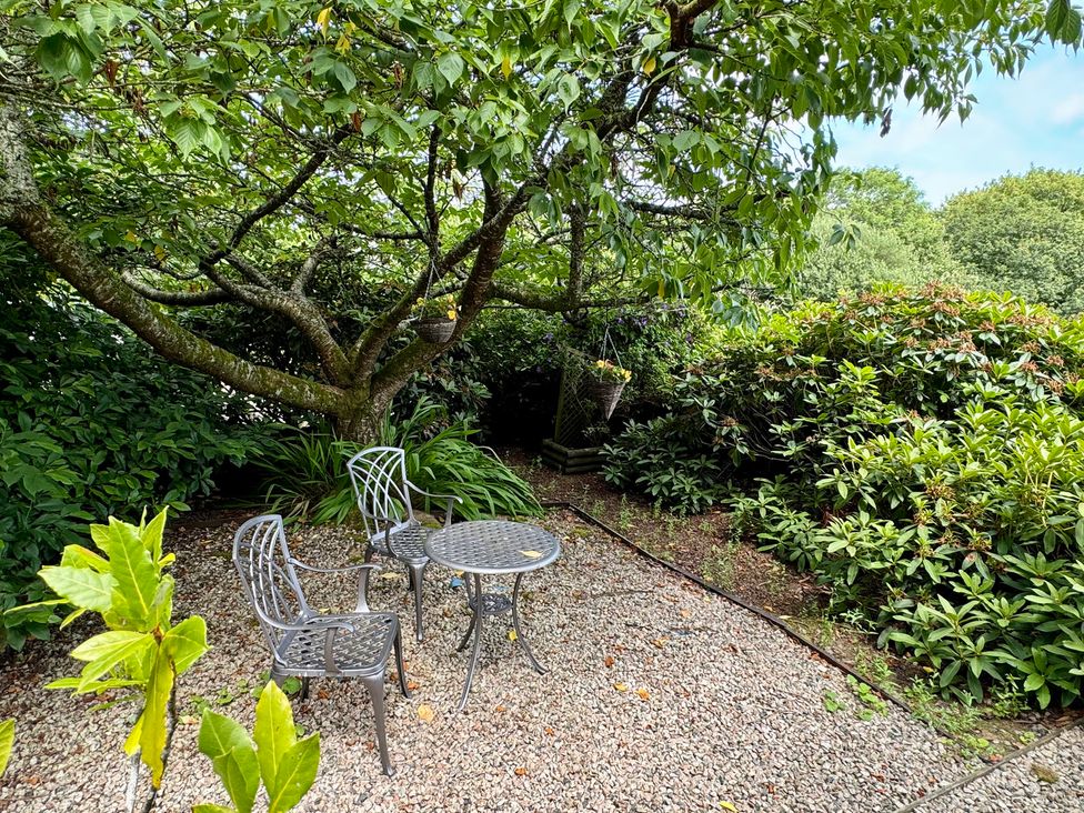 A garden area with table and chairs surrounded by greenery at The Hayloft in Lostwithiel