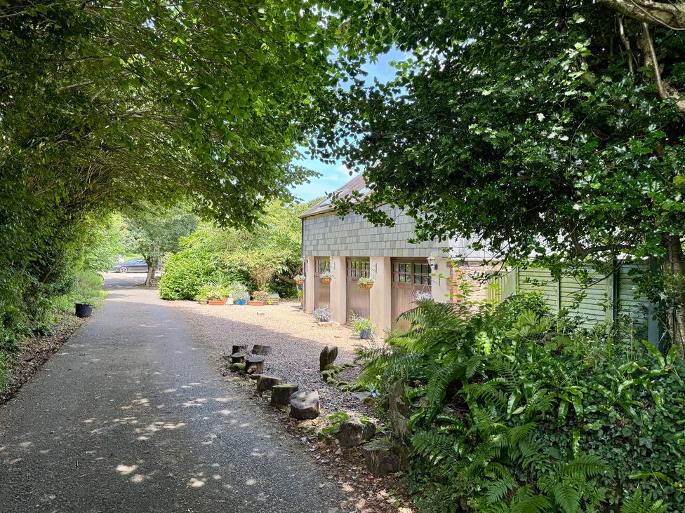 A driveway leading to a garage with trees and flowers at The Hayloft in Lostwithiel