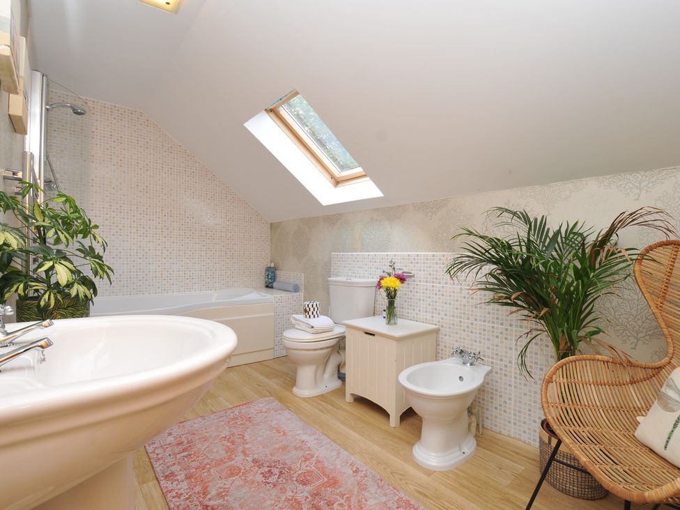 A bathroom with a bathtub, sink, toilet, and chair at The Hayloft in Lostwithiel