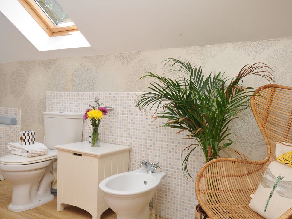 A bathroom with a toilet, bidet, sink, and chair at The Hayloft in Lostwithiel