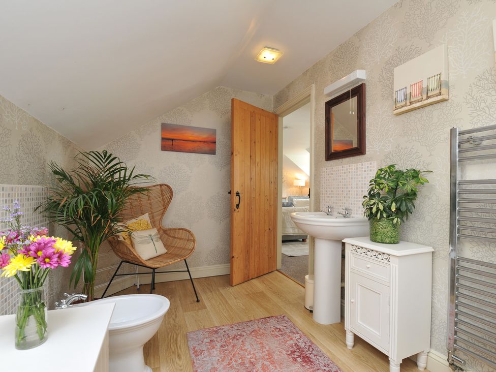 A bathroom with a toilet, sink, and chair at The Hayloft in Lostwithiel