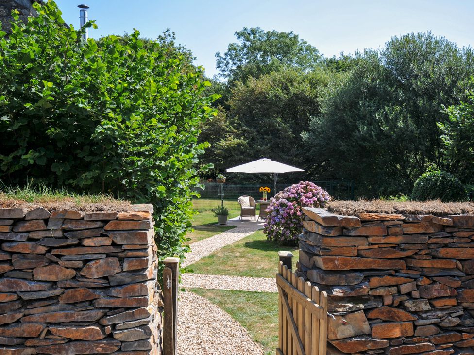 A garden with a stone wall and path leading to an umbrella and chairs at The Mill in Lostwithiel
