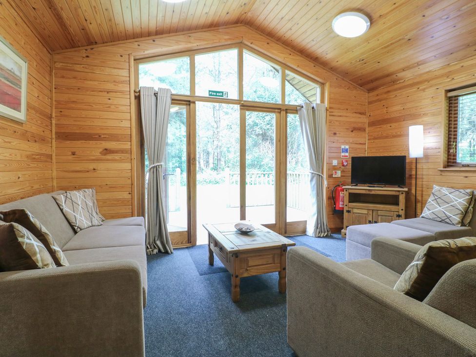 A living room with sofas coffee table television and large windows at Rowan Lodge in Rosliston