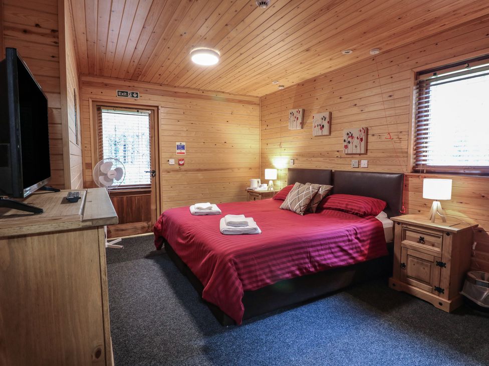A bedroom with a double bed red bedding wooden furniture and a door at Rowan Lodge in Rosliston