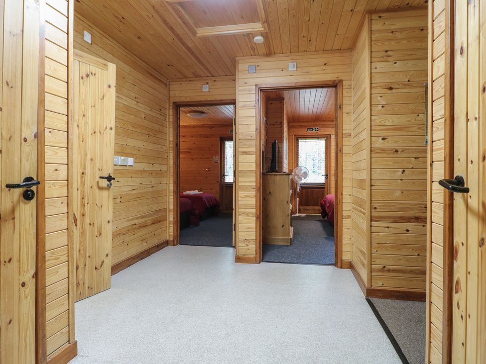 A corridor with wooden walls and ceiling leading to bedrooms with red bedding at Rowan Lodge in Rosliston
