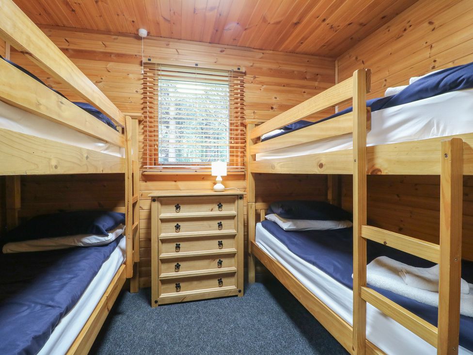 A bedroom with two wooden bunk beds a chest of drawers a lamp and a window at Oak Lodge in Rosliston