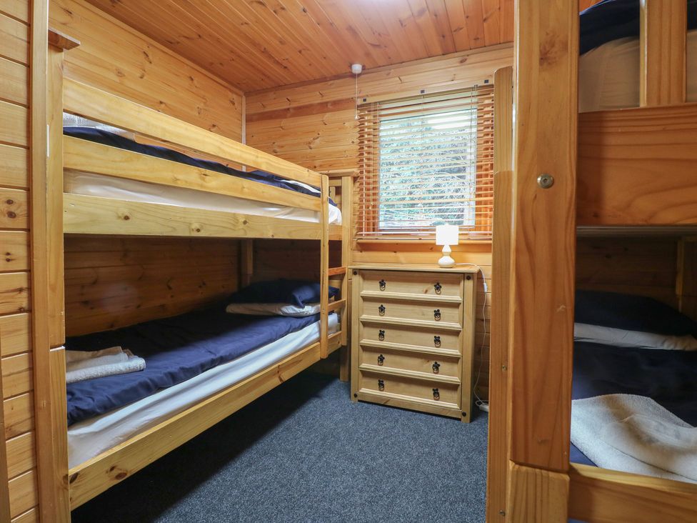 A bedroom with bunk beds a chest of drawers and a window with blinds at Oak Lodge in Rosliston