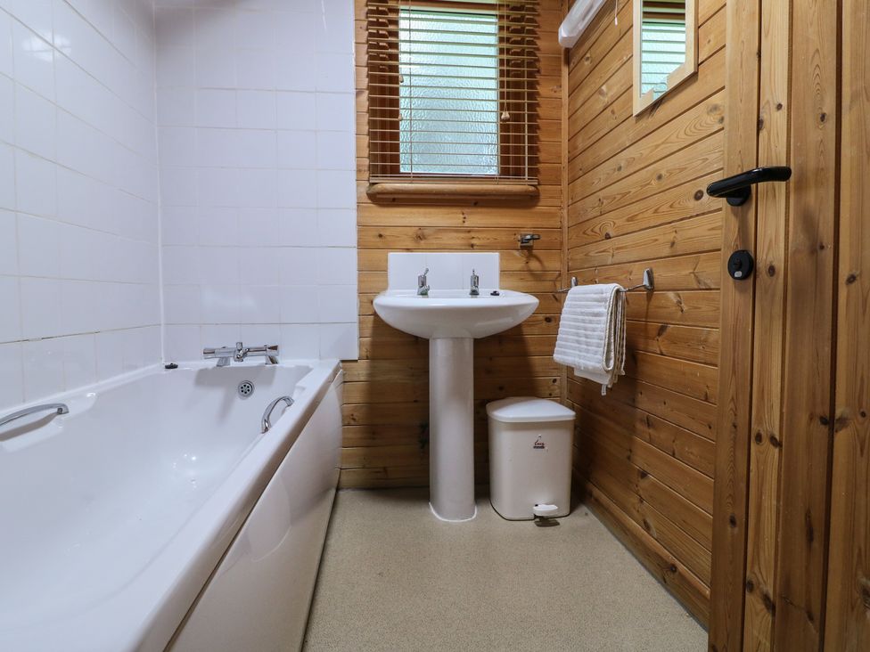 A bathroom with a bathtub sink towel rail and wooden walls at Oak Lodge in Rosliston