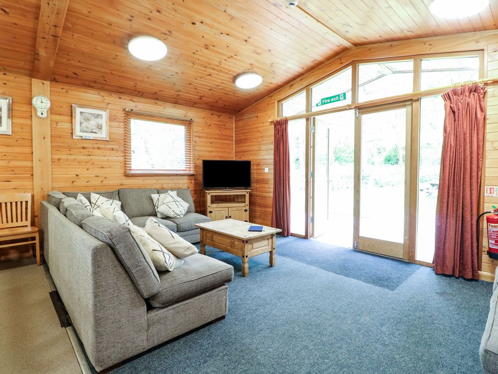 A sitting area with gray sofas a wooden coffee table and a television in a wooden room at Chestnut Lodge in Rosliston
