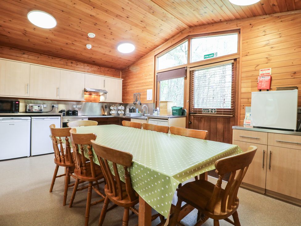 A kitchen with wooden chairs around a table covered with a green polka dot tablecloth at Chestnut Lodge in Rosliston