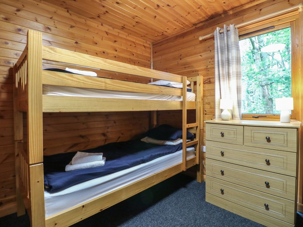 A bedroom with wooden bunk beds and a chest of drawers next to a window with curtains at Chestnut Lodge in Rosliston