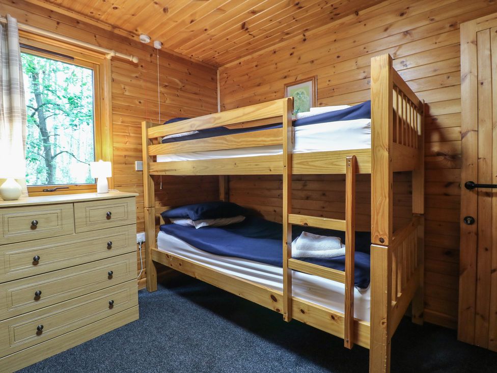 A bedroom with wooden bunk beds and a chest of drawers next to a window at Chestnut Lodge in Rosliston