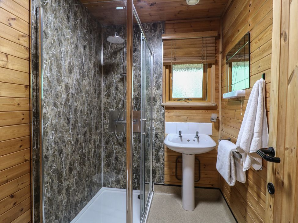 A bathroom with a glass shower enclosure a white pedestal sink wooden walls and a window at Chestnut Lodge in Rosliston