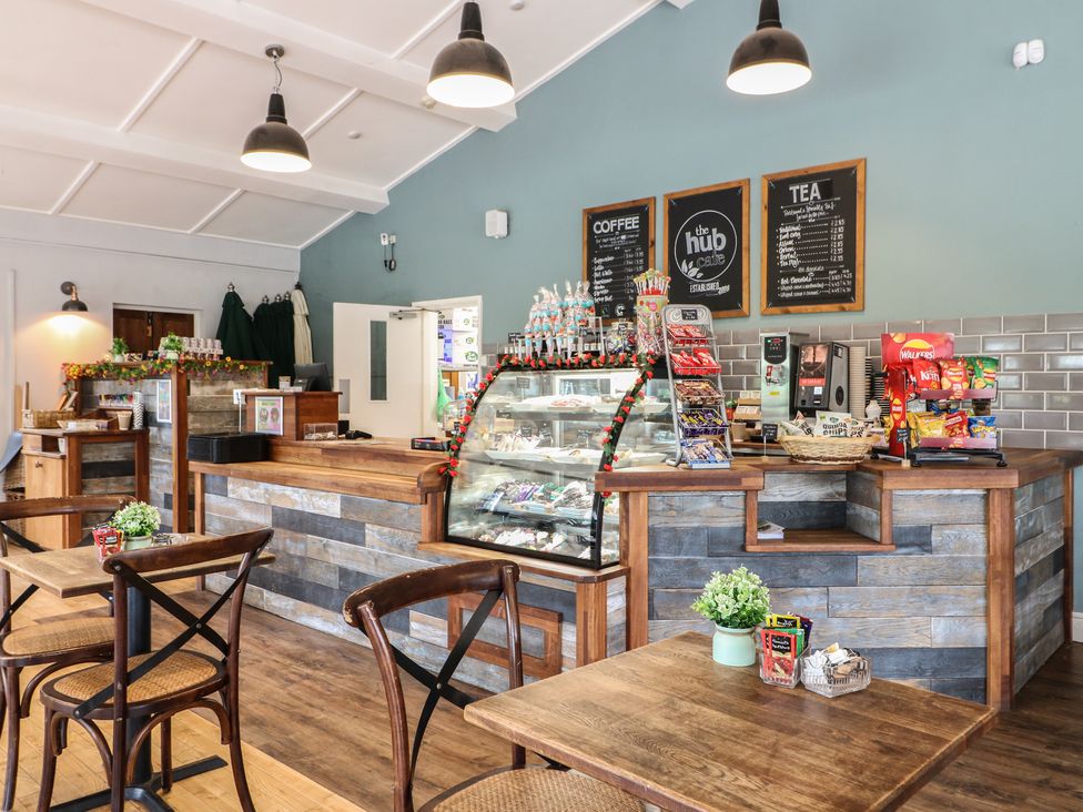 A cafe counter with display case snacks and menu boards with tables and chairs at Chestnut Lodge in Rosliston
