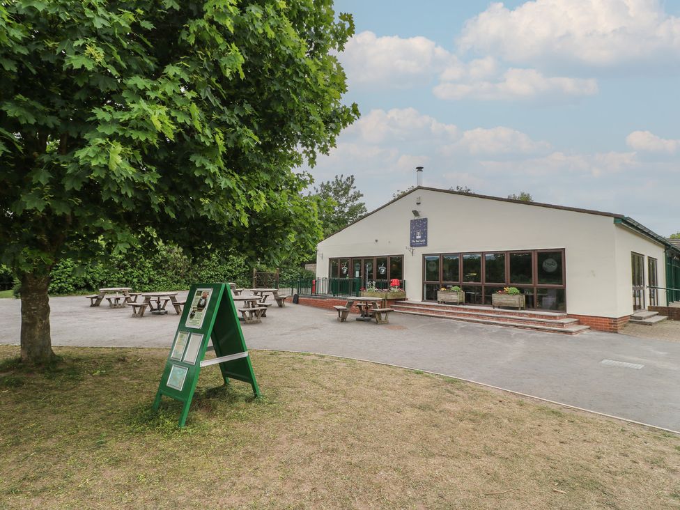 An outdoor area with picnic tables a green signboard and a white building with large windows at Chestnut Lodge in Rosliston