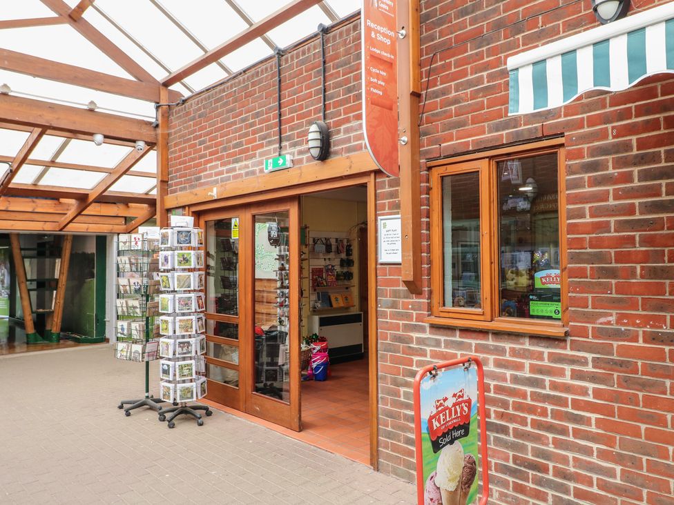 A covered outdoor walkway with a brick wall shop entrance displaying postcards and an ice cream sign at Chestnut Lodge in Rosliston
