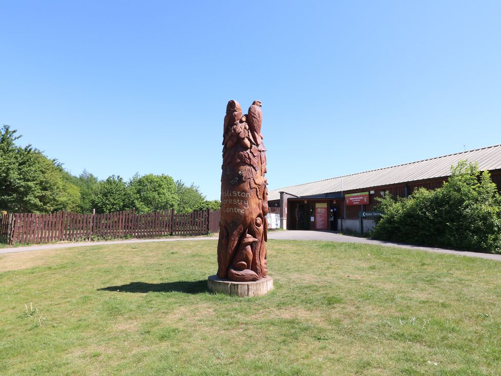 A wooden sculpture on grass near a building and a fence at Rosliston Forestry Centre