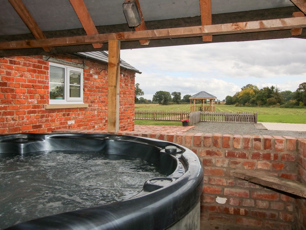A hot tub near a brick wall with a view of a gazebo in the field at Millstone Cottages - Millstone Cottage Westbury