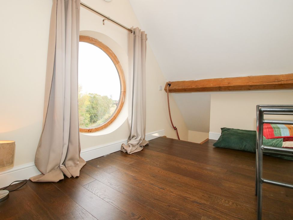 A loft with a round window and a beam at Millstone Cottages - Breidden View in Westbury