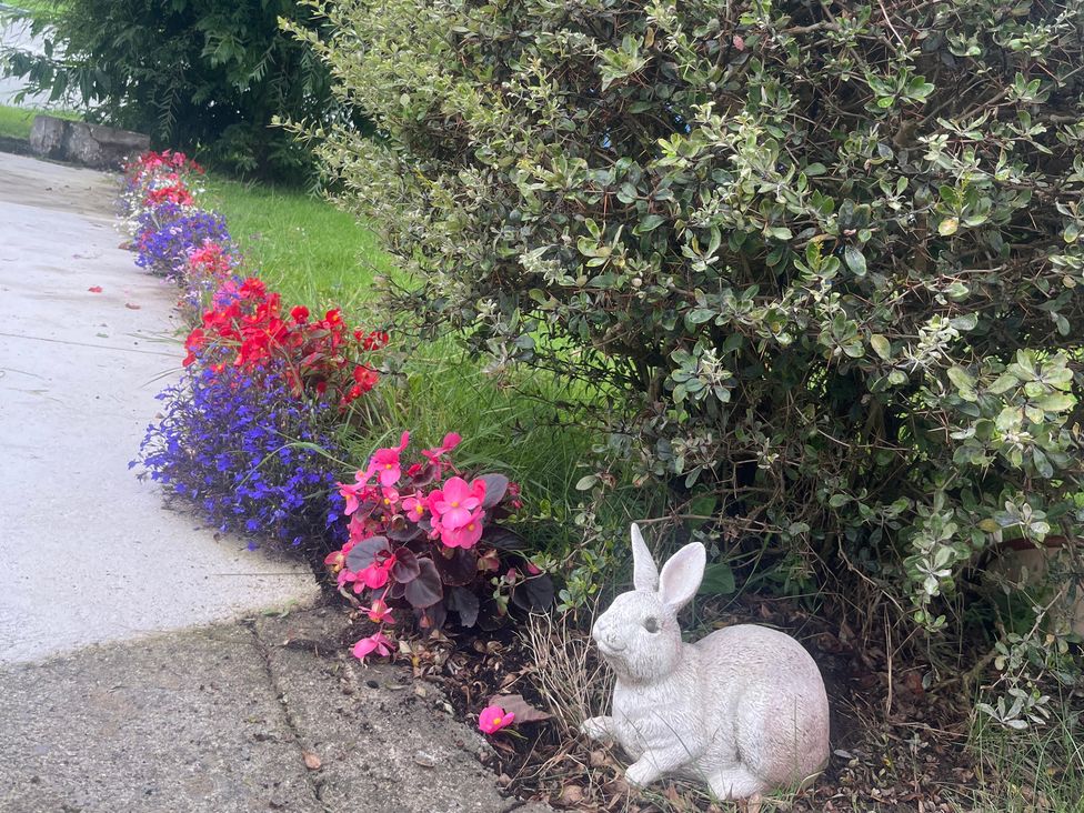 A flower bed with red, blue, and pink flowers and a rabbit statue at Dromclough Farmhouse Dromclough near Listowel, County Kerry