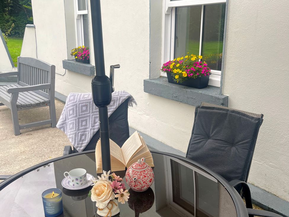 A table with a book, teapot, cup, and flowers on an outdoor patio at Dromclough Farmhouse in Dromclough near Listowel, County Kerry