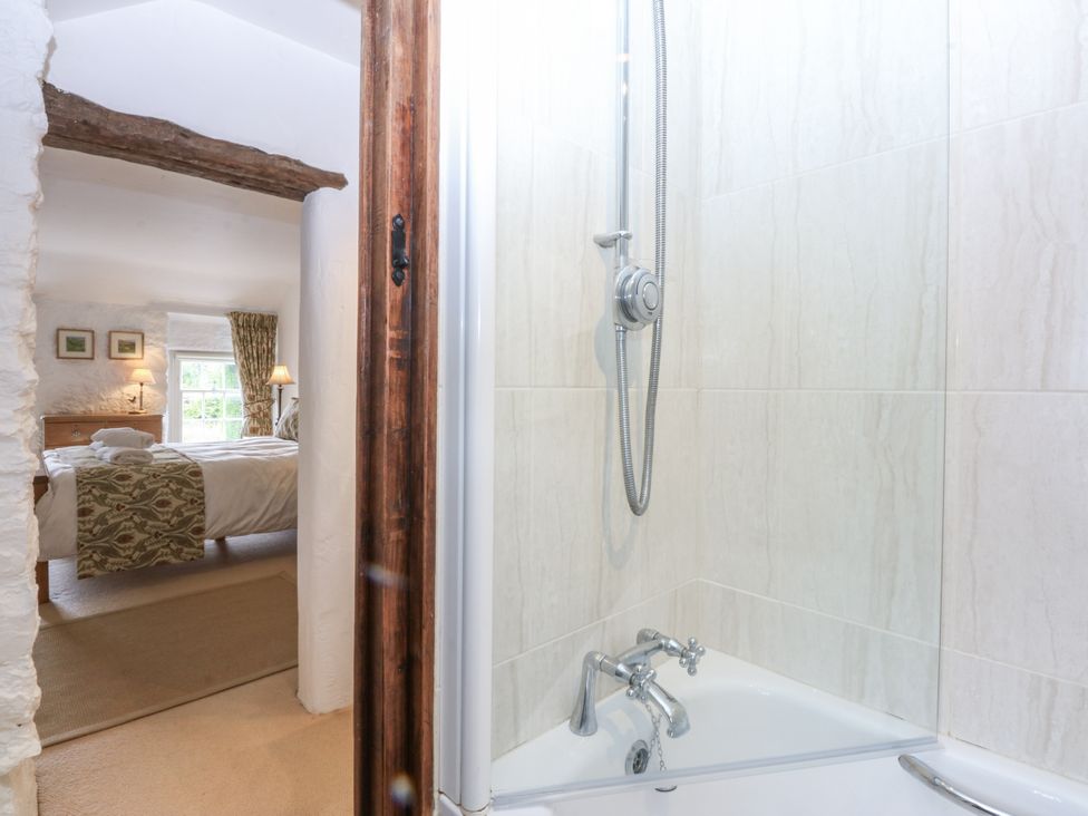 A bathroom with a bathtub and shower looking into a bedroom at Tyddyn Iolyn in Benllech