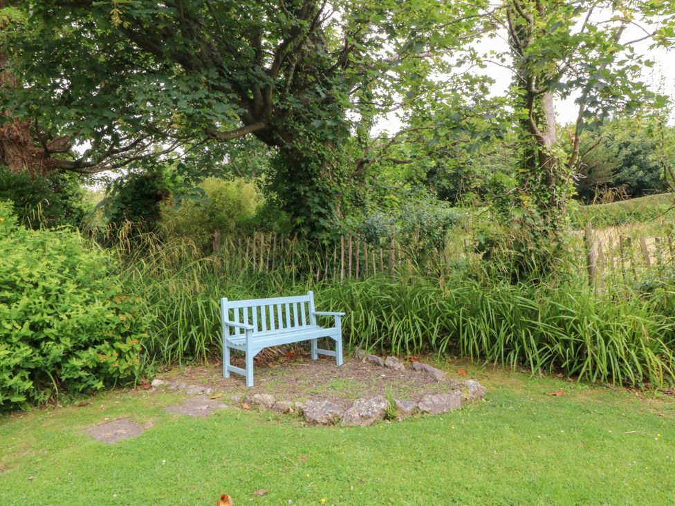A garden with a bench surrounded by grass and trees at Tyddyn Iolyn in Benllech