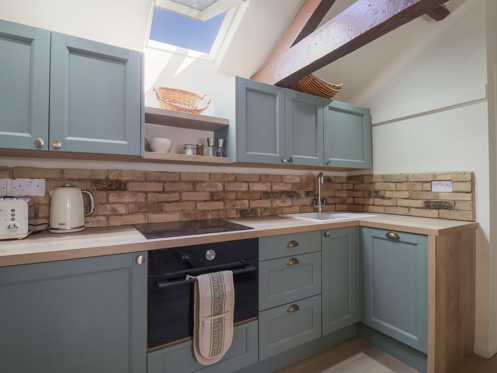 A kitchen with blue cabinets a brick backsplash a stove an oven a kettle a toaster and a sink at Drakes Hideaway in Lyme Regis