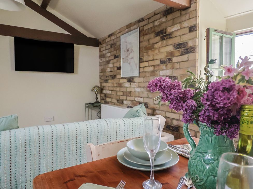 A dining table with tableware and a green vase of flowers next to a sofa and a wall mounted tv in a living room at Drake's Hideaway in Lyme Regis