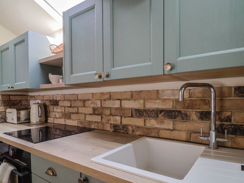 A kitchen with blue cabinets a brick backsplash a sink and a countertop with a kettle and toaster at Drake's Hideaway in Lyme Regis