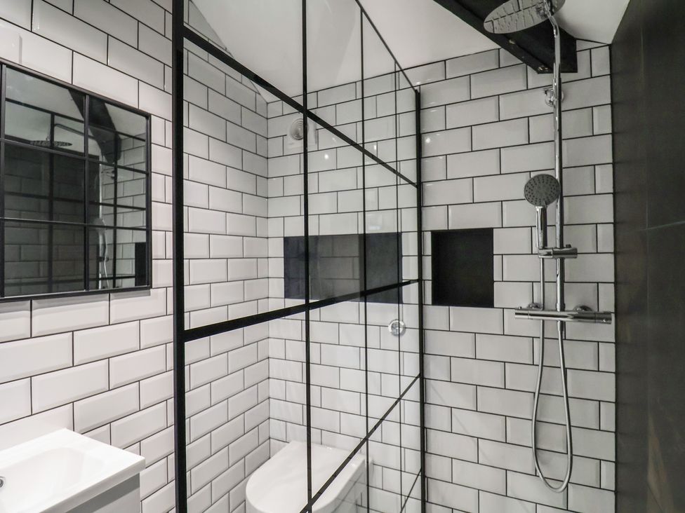 A bathroom with white tiled walls a shower area with a glass partition and a mirror at Drakes Hideaway in Lyme Regis