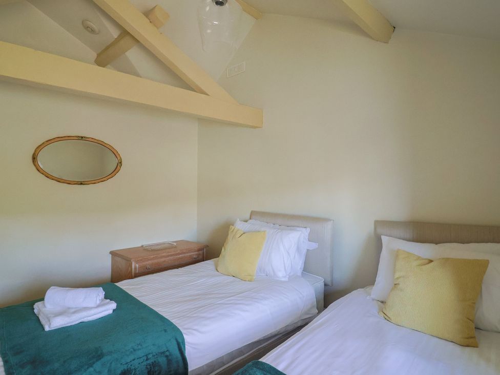 A bedroom with two single beds with yellow pillows and a wooden dresser under an oval mirror at Drakes Hideaway in Lyme Regis