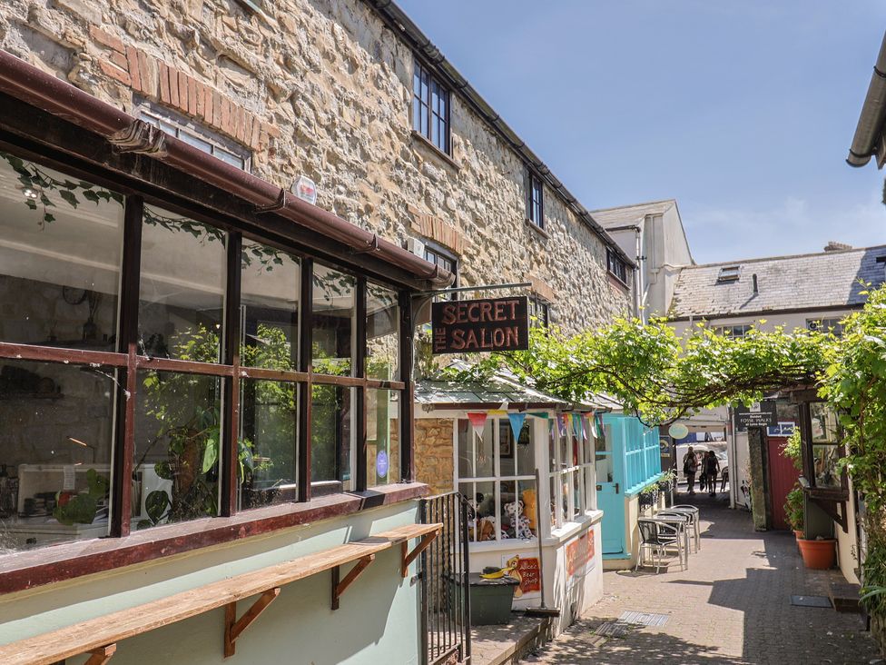 An outdoor alley with stone buildings tables and chairs a sign reading Secret Salon and plants overhead at Drakes Hideaway in Lyme Regis