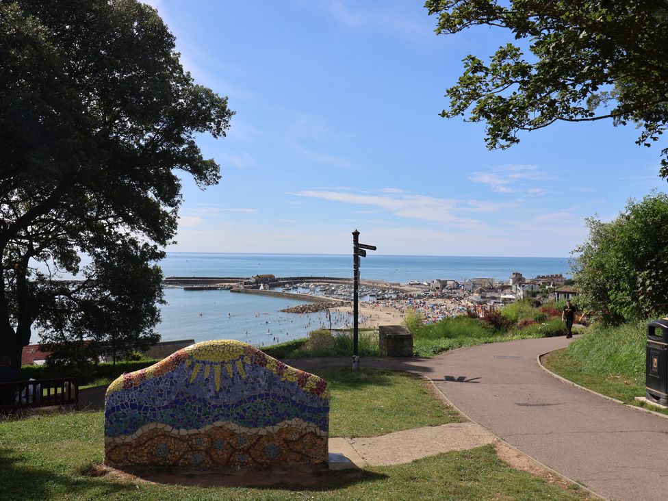 A coastal view with a mosaic bench a path trees and a beach in the background at Drakes Hideaway in Lyme Regis