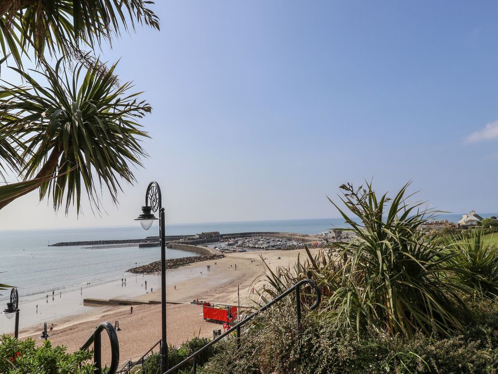 A beach with people walking near the sea and a marina with boats in the distance at Drakes Hideaway in Lyme Regis