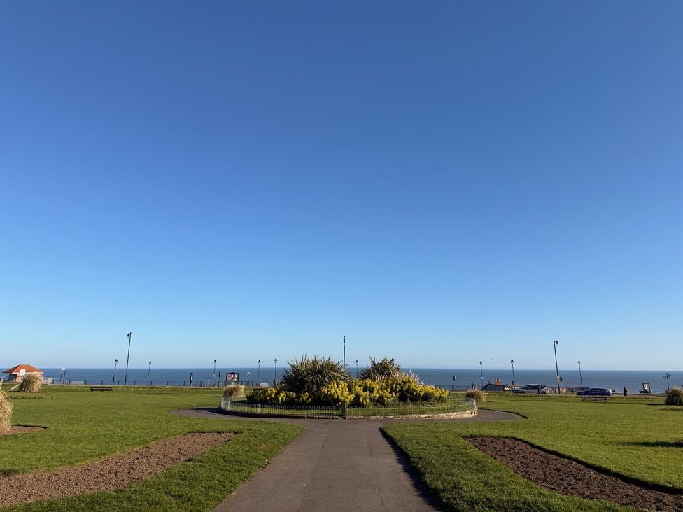 A pathway leading to a flower bed with the ocean in the background at Pebble Cottage in Whitby
