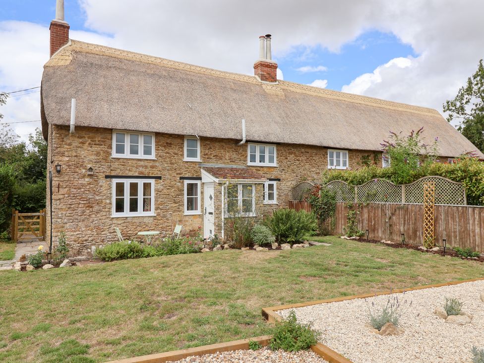 A stone cottage with a thatched roof and garden at Thatchers End, Sherborne