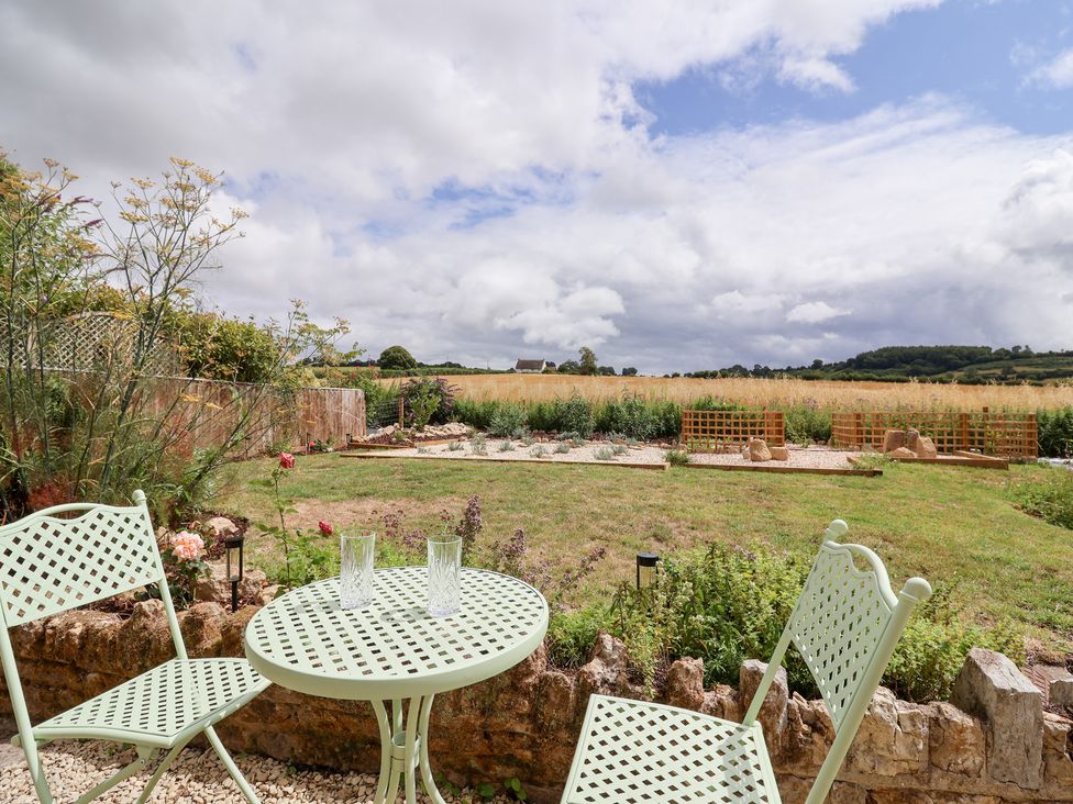 A garden with a table and chairs overlooking a field at Thatchers End in Sherborne
