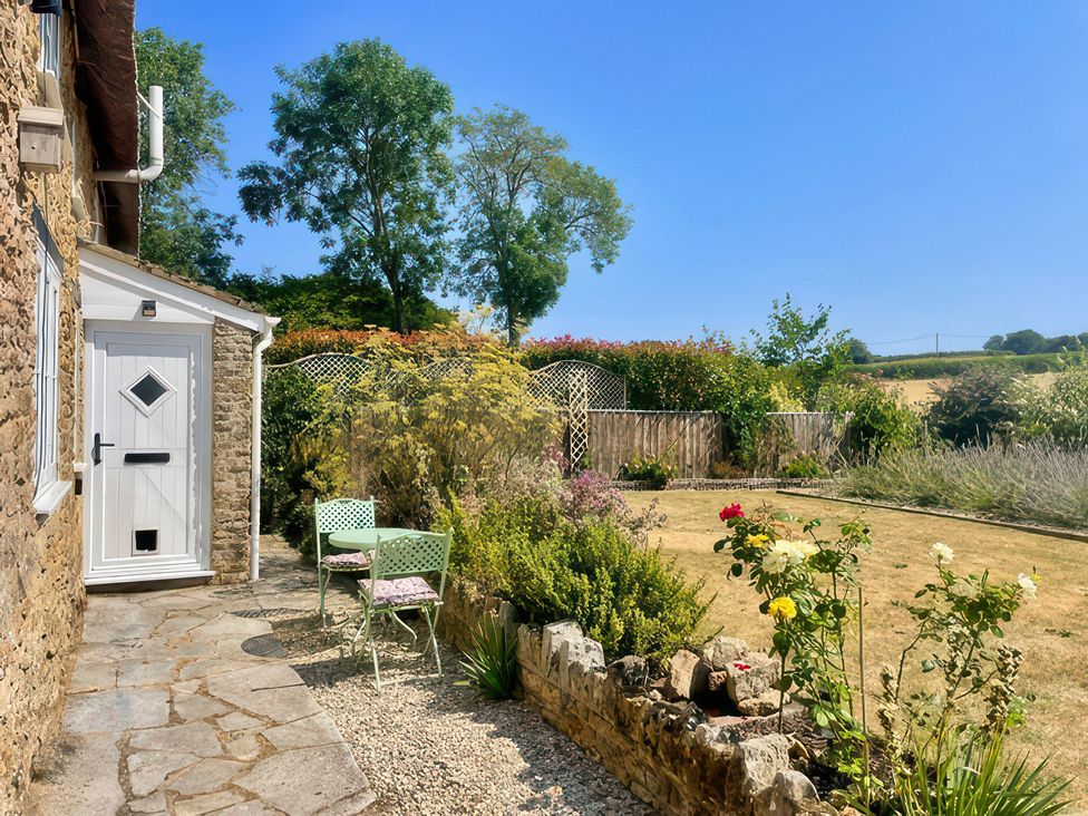 An outdoor space with a table and chair near flowers at Thatchers End in Sherborne