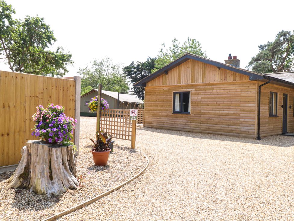 An outdoor view of a wooden house with a garden and gravel path at Rabbit Warren Lodge in Snettisham