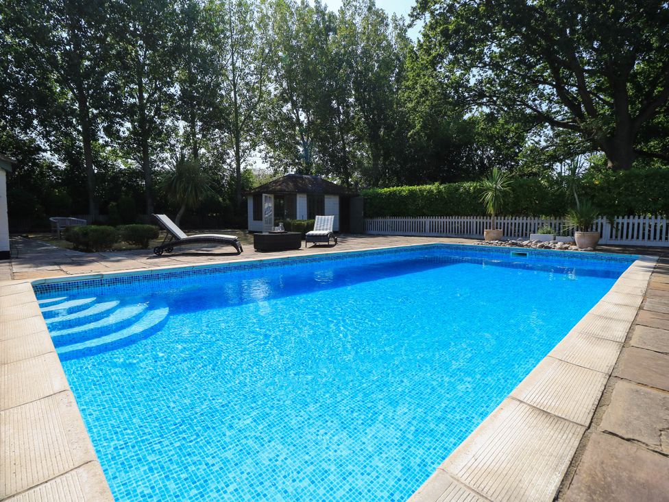 A swimming pool with deck chairs and a garden shed at Beam Cottage in Warsash