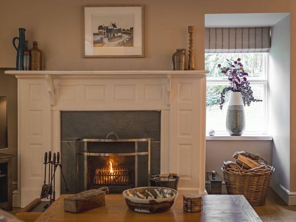 A living room with a fireplace and flowers in a vase at Tan Llan in Llanelltyd near Dolgellau