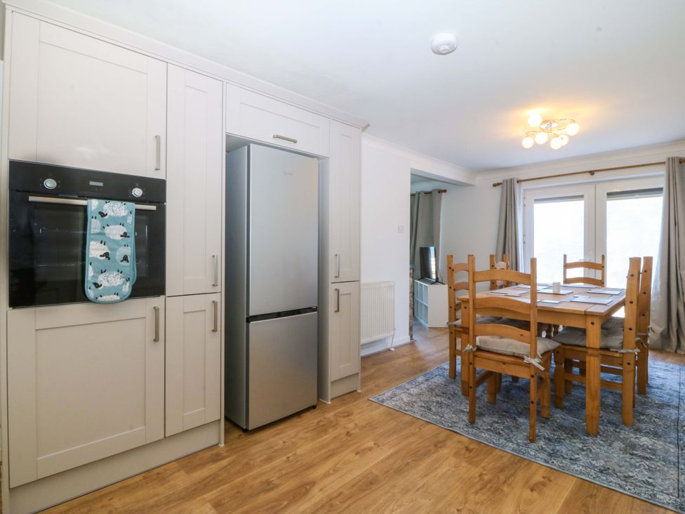 A kitchen with an oven, refrigerator, and dining area at 20 Gwelfor Estate Cemaes Bay