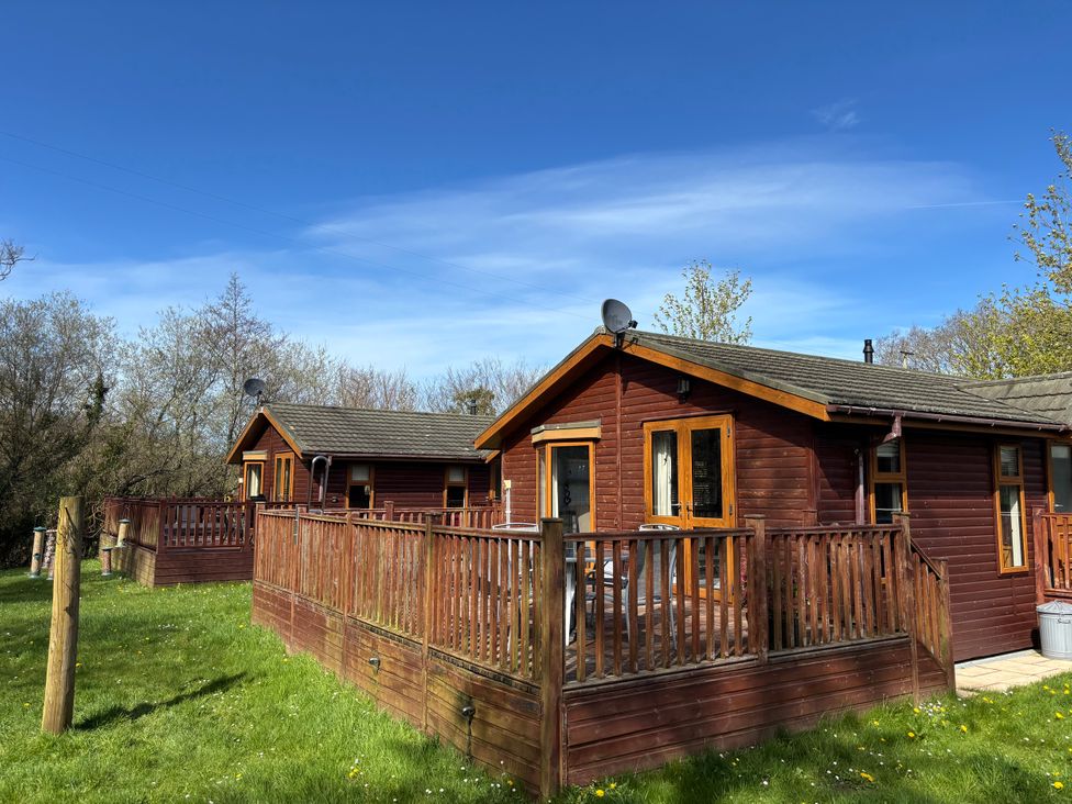 Two log cabins with wooden decks and satellite dishes at 2 Riverside Lodge Abercych near Cenarth