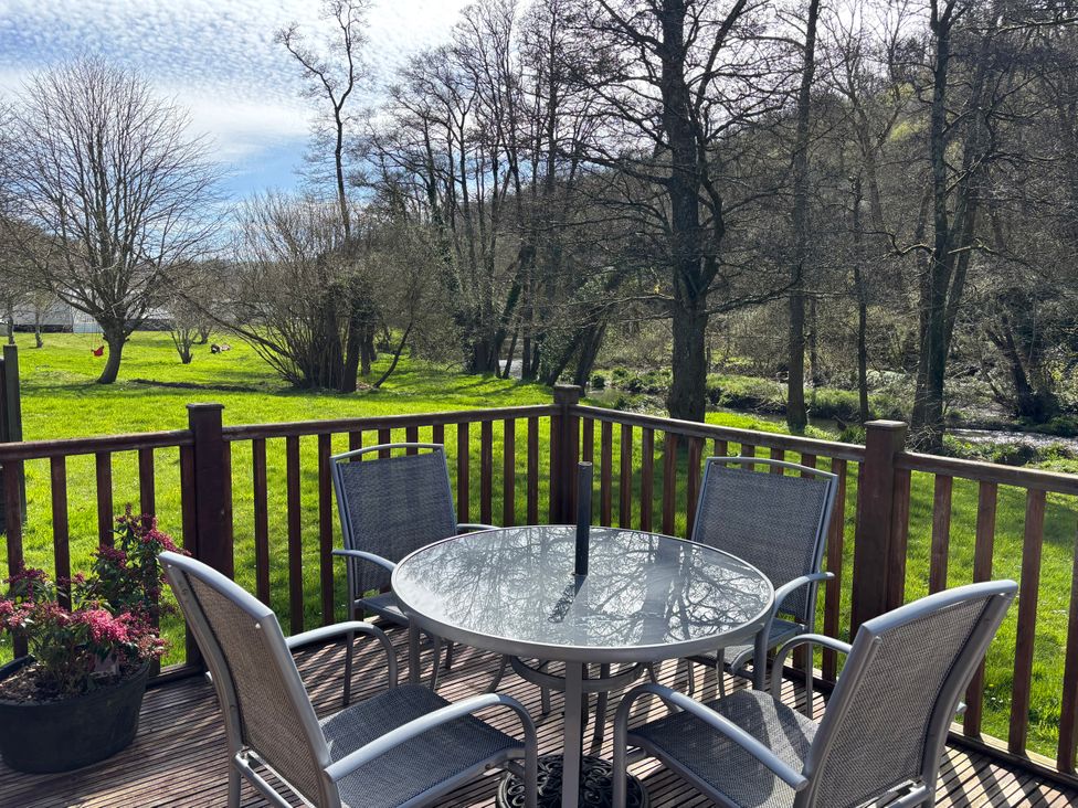A table and chairs on a deck at 2 Riverside Lodge in Abercych near Cenarth