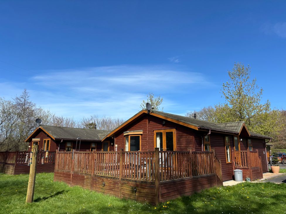 Wooden lodges with decking in a garden at 2 Riverside Lodge Abercych near Cenarth