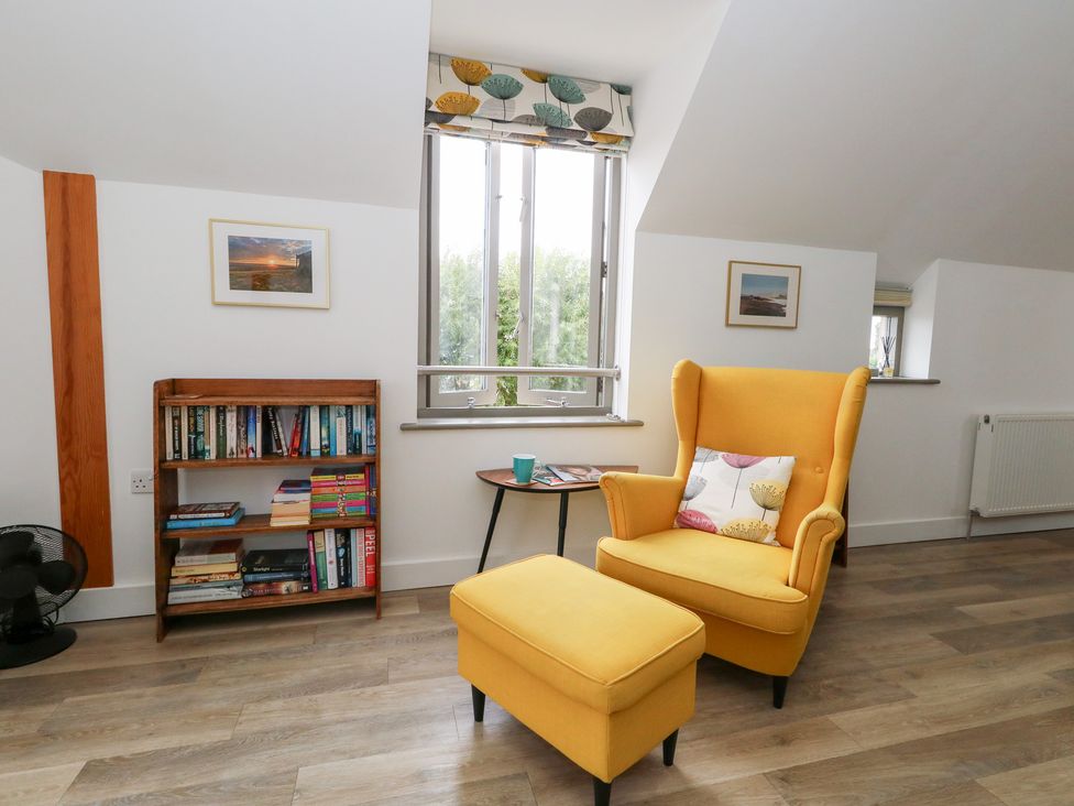 A living room with books on a shelf and a yellow armchair at Coastguard Lookout in Wyke Regis