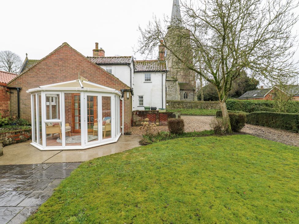 A garden with a conservatory and a church in the background at White Gates in Banham