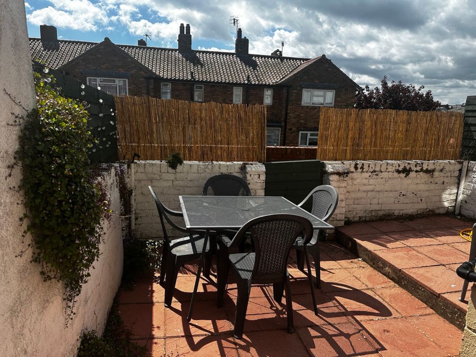 An outdoor patio area with a square table and four chairs surrounded by low white walls and bamboo fencing at Launchers Cottage in Scarborough