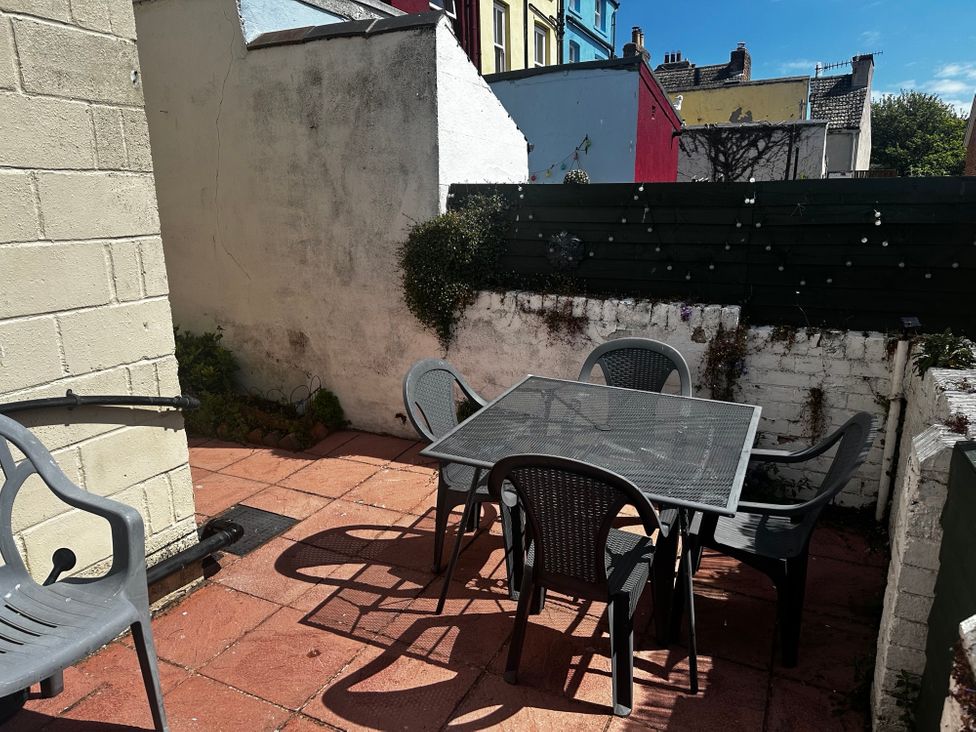 An outdoor patio with a metal table and four plastic chairs surrounded by white and dark green walls at Launcher's Cottage in Scarborough
